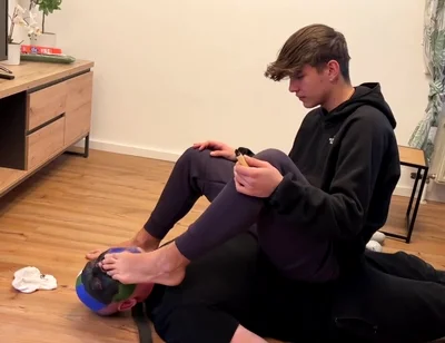 German master sitting on feet licking boy